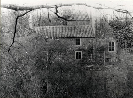 Photograph of the exterior of a two-storied building with the branches of a tree in the foreground; the building has been identified as Mill Farm, Hawthorn