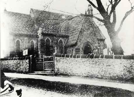 Photograph showing the exterior of the west wall and porch of the parish church at Hawthorn, taken from the north-east and showing part of the churchyard wall and the gate to the churchyard; part of the handlebars of a bicycle can be seen on the extreme left of the picture can be seen