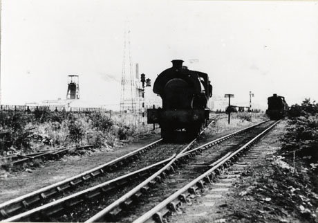 Photograph of the front of two locomotives running along tracks towards the camera; the tracks cross at the front of the picture; in the background the winding gear and surface buildings of a colliery may be seen; the photograph has been identified as depicting Hawthorn Coking Plant