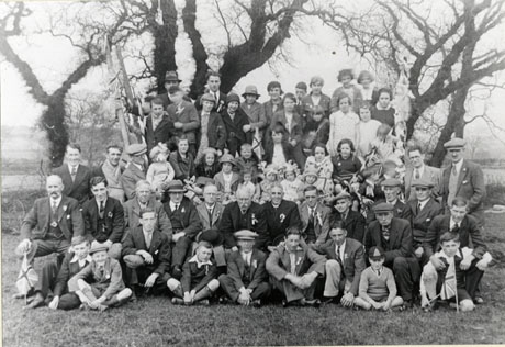 Photograph of a group of approximately sixty people posed in front of trees; the people are comparatively formally dressed in overcoats, dresses, suits, and hats; the group has been identified as marking the celebrations in Hawthorn of the Silver Jubilee of the reign of King George V