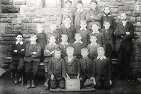 Photograph of a group of twenty boys posed outside a stone building with a man, presumably a teacher; a boy on the front row holds a notice reading: Hawthorn School 1910 Class 1