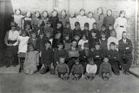 Photograph of a group of forty three children of varied ages posed against the wall of a stone building with a man and a woman; a child at the front of the group is holding a notice which reads: Hawthorn School 1921