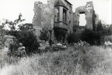 Photograph showing a ruined wall with a ruined bay window and a ruined wall at right angles with an empty window space; in front of the ruins long grass and wild flowers can be seen and two small boys are standing at the left of the photograph near the wall; the ruins have been identified as The Remains of Hawthorn Towers, August 1966