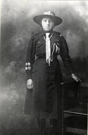 Photograph, full-length, of a girl wearing the uniform of the Girl Guides; she has four badges on her right sleeve and two stripes on the left pocket of her blouse; the photograph appears to have been taken in a photographer's studio; the girl has been identified as Miss Jennie Haythorne of Hawthorn Village