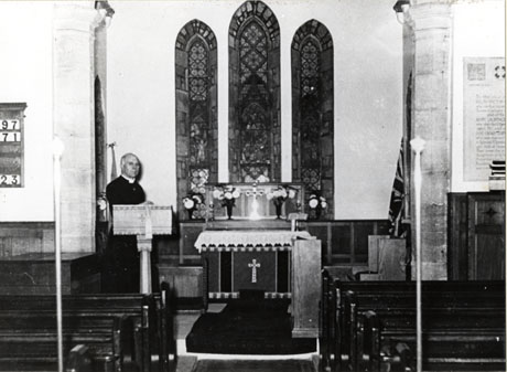 Photograph of the interior of Hawthorn church showing the altar, east windows, first four pews and the lectern; a clergyman, identified as Rev. Moore, can be seen standing at the lectern