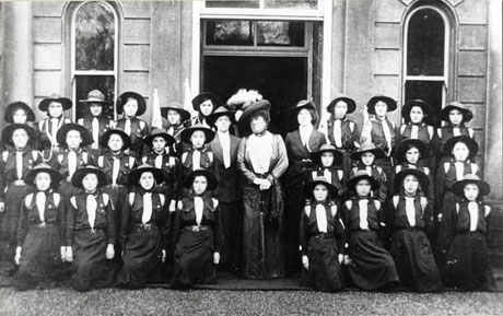 Photograph of a group of twenty seven Girl Guides posed in front of a large building with an imposing doorway; the Guides are described as Hawthorn and Seaham Guides and are accompanied by Lady Londonderry in the centre of the group with Miss Dillon on her left and Miss Pemberton on her right