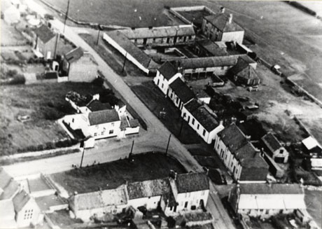 Photograph taken from the air showing a street running from bottom right to top left of the photograph with another street running into it from the left; both streets are lined with houses; behind the houses lining the streets there appears to be open country; the settlement has been identified as Hawthorn Village