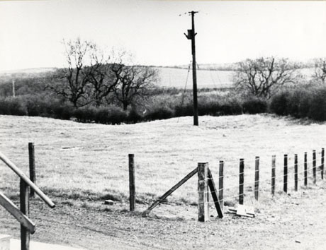 Photograph of a piece of open ground with a telegraph pole and a fence enclosing the ground; in the distance further fields can be seen; the photograph has been identified as Monk Hesledon, after the bulldozers, presumably showing the area previously occupied by the cottages in hesl0012