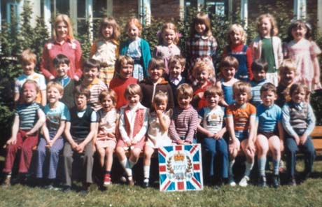 Photograph of twenty eight children, aged approximately six years, posed in three rows outside a building; a woman is standing with them; in front of them is a board with the symbol of the Silver Jubilee of Queen Elizabeth II in 1977; thay have been identified as a class in an Infants' School in Hesledon