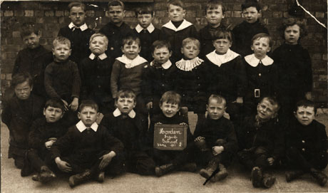Photograph of a group of twenty two boys and one girl posed in front of a brick wall; a boy on the front row is holding a notice reading: Hordern Infants' School 549a Cl 2