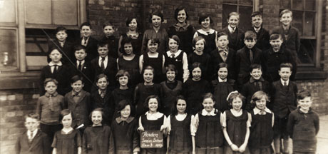 Photograph of forty children posed in front of a brick building; a girl on the front row is holding a notice reading: Horden Senior School Class 3 1927