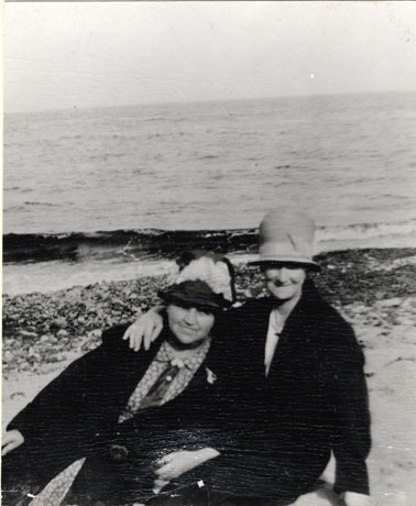 Photograph, close up, of two unidentified middle-aged ladies on a beach, near the shore line; they are wearing coats and hats; the beach has been identified as being at Horden