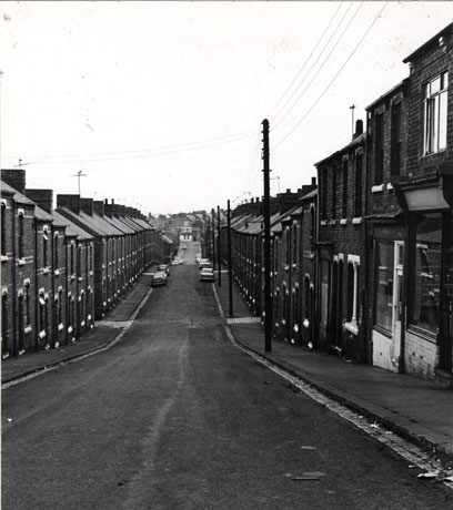 Photograph looking downhill along a road lined on both sides with terraced houses; eight cars can be seen parked in the distance on the road; the road has been identified as 3rd Street, Horden