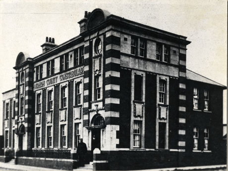 Photograph of the exterior of a building, built of brick with stone details, showing its front and side; across the front is written Durham County Constabulary; an indistinct policeman can be seen standing on the steps of one of the entrances to the building, which has been described as now Comrades Club