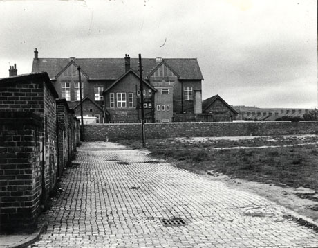 Photograph of the rear of a building, with half timbering, in the distance, described as the Workmen's Club, Hordern; to the left of the photograph the rear of buildings can be seen along with the surface of a brick road leading past them; on the right of the photograph an open space and the chimneys of a row of houses can be seen