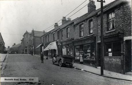 Postcard photograph entitled Blackhills Road, Horden. 5470, showing the right-hand side of a road running downhill towards the camera; the facades of shops can be seen, including that of F. Cowley, Fancy Dealer, and that of Gales's Bazaar; at the top of the hill a large building identified as The Empress Cinema can be seen; a girl standing in the road and a woman in the doorway of F. Cowley's shop can be seen, as can also a motor car, registration number BL5489, parked outside F. Cowley