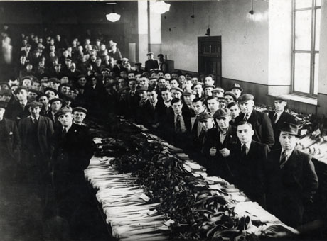 Photograph showing the interior of a hall described as the Working Mens' Club, Horden, with a table, the length of the room, covered in leeks, for the Leek Show, surrounded by men wearing for the most part suits and ties