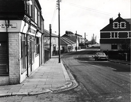 Photograph showing a road leading away from the camera and bearing slightly to the right; the left-hand side of the road can be seen with the premises of Young's Off Licence nearest to the camera; beyond that are other shops, with semi-detached houses in the distance; on the right-hand side of the road, the end of a large building can be seen; a car is parked in the road; the photograph has been identified as Cotsford Lane Viewing Windsor Terrace Horden