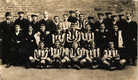 Photograph of ten members of the Horden Colliery Football Team, accompanied by eighteen other men and boys, posed in front of a brick wall; one of the players is holding a ball reading:Horden Colliery A. F. C. 1911- 1912