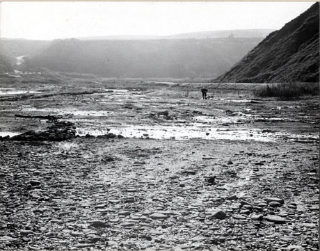 Photograph of the beach looking inland with hills in the distance; a man can be seen in the distance on the shore bending over; the foreground of the picture shows the surface of the beach clearly; the photograph is described as Dene Holme Horden