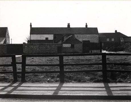 Photograph of the exterior of a farm building, behind a wall, beyond a strip of grass, behind a fence in the foreground of the photograph; the farm has been identified as Cowans Farm(Now Kings) 1976