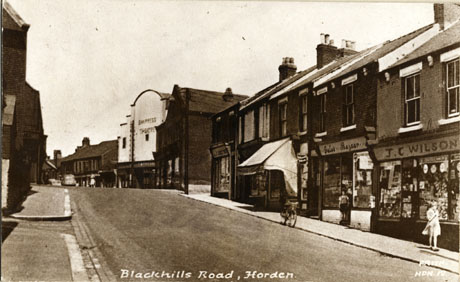 Postcard photograph entitled Blackhills Road, Horden. Frith HDN. 12 showing the facades of the shops at the brow of the right-hand side of the road; those identifiable are: Carruthers; Gales' Bazaar; J. and C. Wilson; the Empress Cinema can be seen at the top of the hill