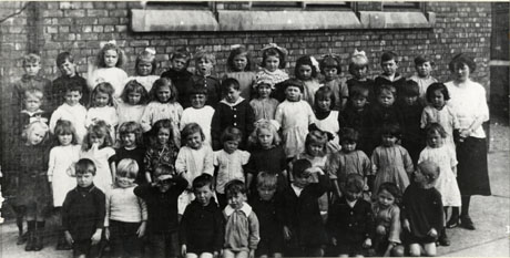 Photograph of forty nine children, aged approximately six years, posed against a brick wall with a woman, presumably the children's teacher; the photograph has been identified as Horden Junior School, Class 8