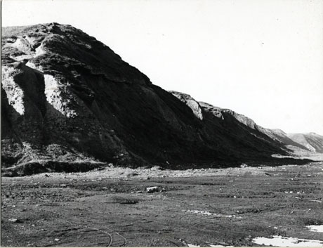 Photograph of the surface of a beach with in the middle distance cliffs and sand dunes; the photograph is identified as Horden Beach 1976