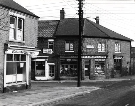 Photograph showing the junction of two roads; on the corner of the road on the left is the Hong Kong Curry House and on the corner of the road on the right is a hardware shop belonging to R. Edwards; the facades of both shops can be seen; the photograph has been identified as Cotsford Lane onto 3rd Street 1976
