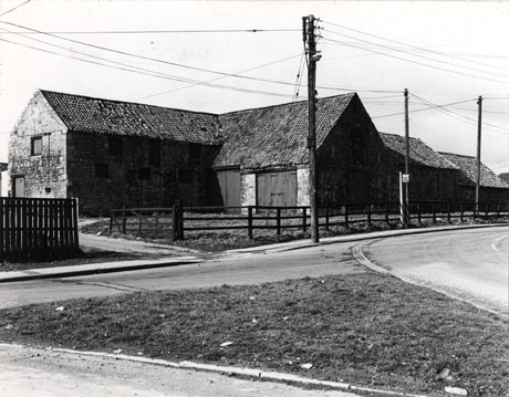 Photograph showing a barn with two wings and two further farm buildings along the road; a road runs in front of the buildings; the photograph is described as King's Farm Yard 1976