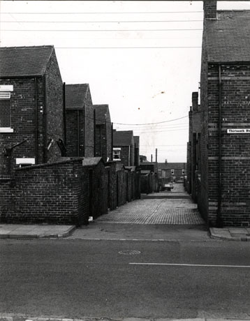 Photograph looking away from the camera, between the backs of terraced houses, to a row of terraced houses on a street in the far distance; on the side of a house on the street closest to the camera the words Thirteenth Street can be seen; the photograph has been identified as South Terrace and Tees Street, Horden