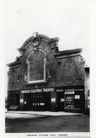 Photograph of the exterior of the Empress Electric Theatre, Horden; the elaborate facade of the cinema can be seen as can the facade of a watch-maker's shop, advertising a watch sale, which forms part of the building