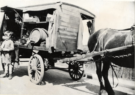 Photograph showing a horse-drawn waggon with a horse between the shafts and a small child standing near the waggon; the side of the waggon is open, revealing a barrel and other unidentified items; the photograph has been identified as Oil and Vinegar Waggon, Horden, 1930s-1940s; the child may have been identified as Charlie Williams