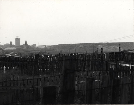 Photograph showing the fences and huts of allotments in the foreground with the spoil heap of the colliery on the right of the picture; the buildings and winding gear of the colliery can be seen in the left of the picture