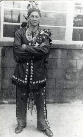 Photograph of a man dressed as a native American with decorated tunic and trousers and feather head-dress; he is standing in front of a building; he has been identified as G. Price in Fancy Dress, Horden Carnival, 1961