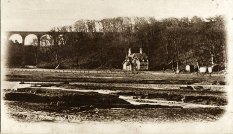 Postcard photograph entitled Dene Holme and Viaduct, showing a viaduct in the far distance and, in the middle distance, the exterior of a house, with steep gables, at the foot of a slope covered in trees