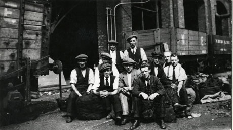 Photograph of ten men in shirt sleeves sitting on the ground in front of coal waggons outside colliery buildings; they have been identified as Horden Colliery Officials during the 1926 Strike