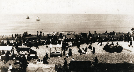 Photograph, looking out to sea, of the beach at Horden; on the beach approximately eight stalls can be seen; in addition, indistinct figures can be seen visiting the stalls; two small boats can be seen out to sea;details of the photograph are extremely indistinct