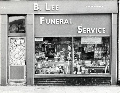 Photograph of the exterior of a shop showing the door and windows which are full of items of hardware; above the window are the following words:B. Lee Hardwaremen Funeral Service; in the window is a notice reading:Funeral Sevice Burials and Cremations Arranged Personnal (sic) Attendance At All Times Funeral Director Mr. B. Lee M.B.I.E.; the shop has been described as Peterlee Funeral Parlour, Horden
