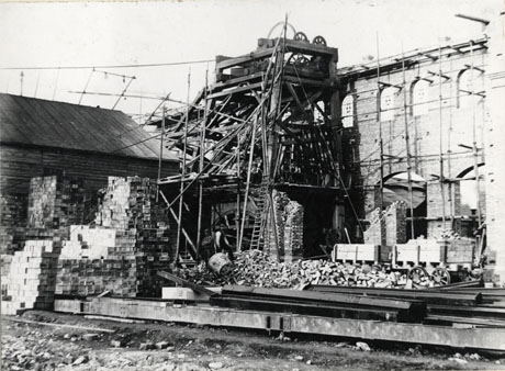 Photograph of the building of the colliery engine house at Horden Colliery, showing at the left, a shed, in front of which, are piles of bricks; in the middle of the picture the winding gear is under scaffold and behind it is a wall of the engine house; in the foreground of the picture are piles of bricks and girders; two indistinct figures can be seen near the scaffolding