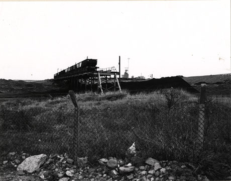 Photograph of railway trucks on a track built above colliery waste; the photograph shows the same picture as 0199, but is taken from further away and shows the same fence as in 0198 and colliery buildings in the far distance