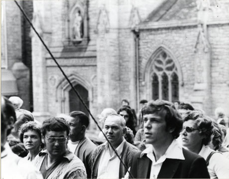Photograph of people in front of St. Nicholas's Church in the Market Place in the City of Durham during the Durham Miners' Gala; a rope can be seen in the foreground of the photograph, which it may be presumed, is attached to a banner