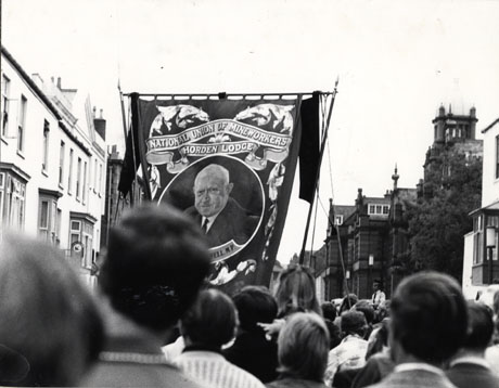 Photograph of the Horden Lodge banner being carried along Old Elvet in the City of Durham during the Miners' Gala; the people carrying the banner have their backs to the camera; the buildings on either side of Old Elvet can be seen; the portrait of Emmanuel Shinwell can be seen on the banner