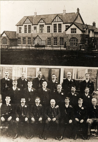 Photograph of the exterior of the Horden Workmens' Social Club; the building has nine windows on the first floor with false half timbering under the eaves; on the ground floor there is a porch and on either side of the building there are two wings at right angles to the building; and photograph of the nineteen members of the first committee of the Social Club, posed outside the building; all the men are formally dressed with flowers in their button holes