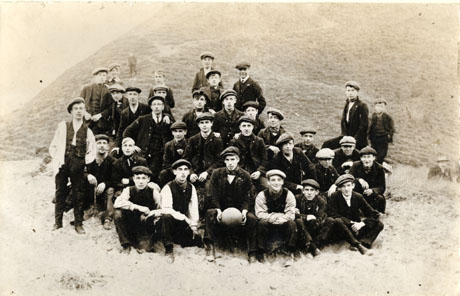 Photograph described as Strikers at Deneholme, Horden, 1926, showing thirty six men and boys in working clothes and caps posed in front of a wooded hillside; man on the front row is holding a football