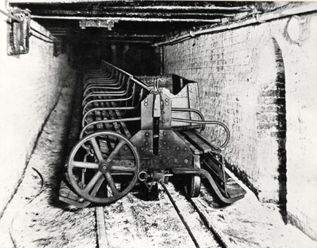 Photograph described as Man Riding Cars, Horden, 1929, showing a roadway underground running away from the camera, with machinery on rails down the centre of the roadway; two very indistinct figures can be seen at the back of the picture