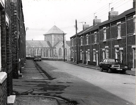 Photograph, looking along a street running away from the camera, with the exterior of a church filling the end of the street; the street has been identified as New 7th Street, Horden and the church as St. Mary's Church, Horden; two cars can be seen parked at the side of the road, the registration of one of which is: MPT 422J