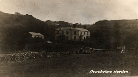 Postcard photograph entitled Deneholme Horden. showing the exterior of a large house with a wooded hillside behind it; to the left of the house is a smaller building and in front of the house is a stone wall; the indistinct figure of a man can be seen in front of the wall