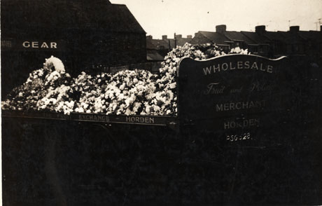 Photograph of the grave of Tommy Gear, Wholesale Fruit and Potato Merchant, Horden, showing the inscriptions on the memorials at the head and foot of the grave; the wreaths given for his funeral are piled on top of the grave