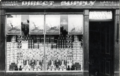 Photograph of a window of a branch of Walter Willson Ltd., showing the following legends above the window Largest Grocers Direct Supply; above the door are the words: Newton House, and piles of goods, including flour, golden syrup, peas and matches, can be seen in the window; also in the window are posters advertising Fighting Tea Sold Only By Walter Willson